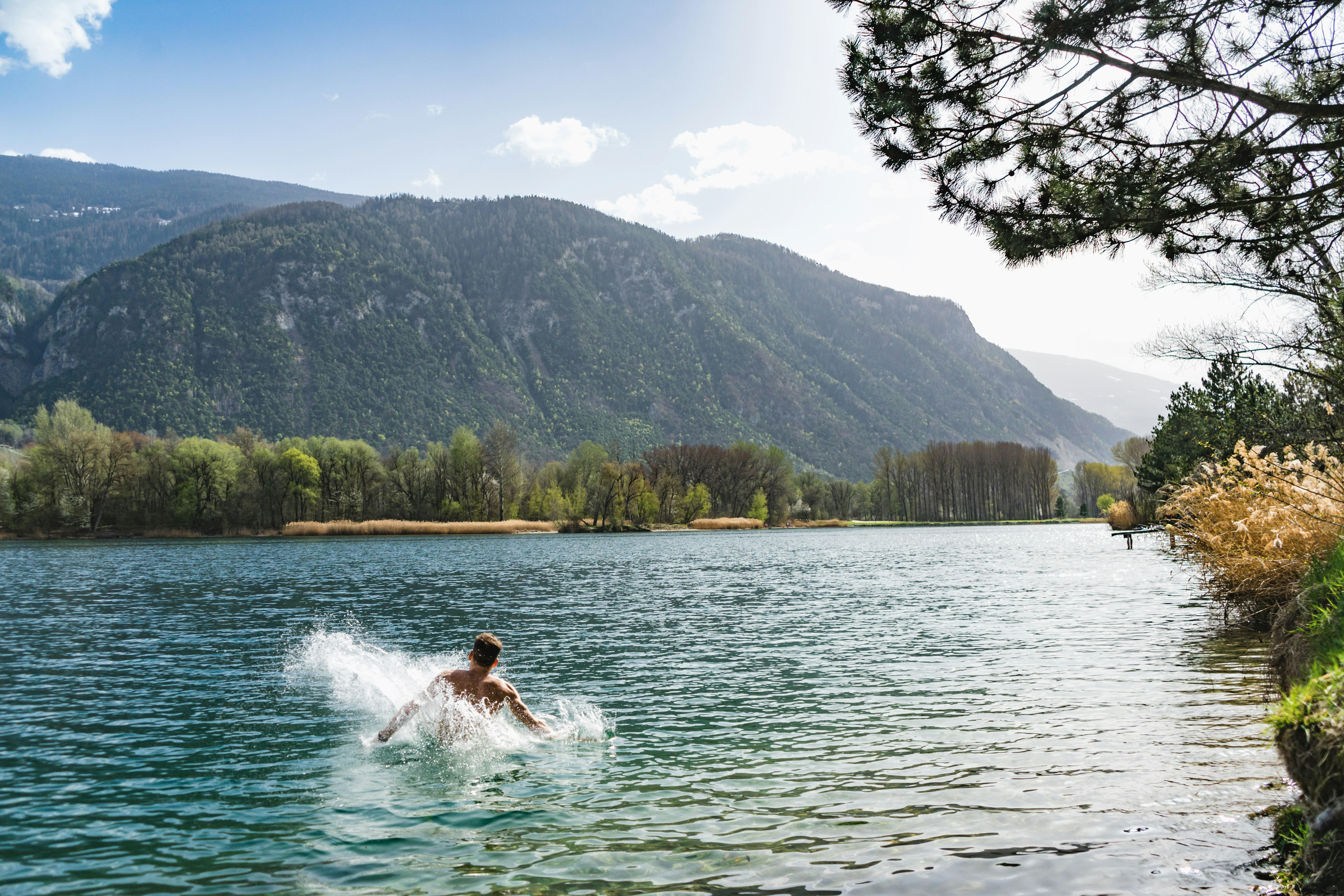 woman in white dress on water near green trees and mountain during daytime